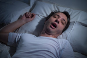 Man sleeping in his bad at night, snoring, mouth open; sleep apnea concept